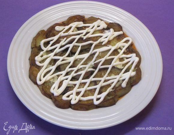 На плоскую тарелку выложить половину остывших обжаренных баклажанов. Сверху выложить тертый чеснок, смазать майонезом.