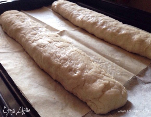 Затем разделить тесто на две части, смазав руки оставшимся растительным масло. И сформировать багеты(просто вытянуть каждую часть багет). Выложить багеты на противень,застеленный бумагой для выпечки и присыпанной чуть мукой. Накрыть багеты полотенцем и дать им отдохнуть еще 15 минут.