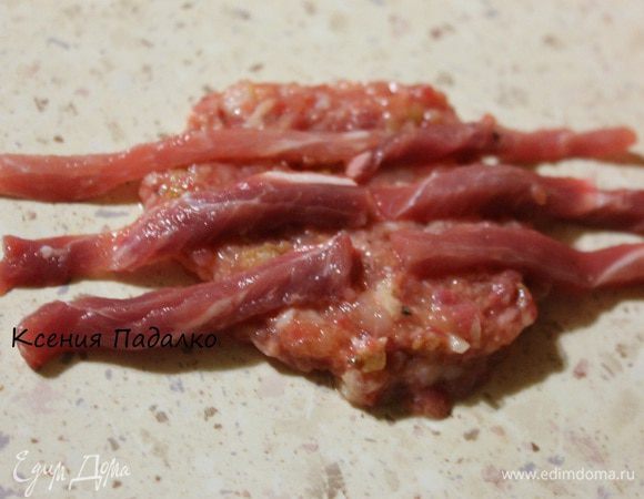 Теперь приступим к сборке паучка. Рабочую поверхность сбрызнуть водой. Кладем сначала тонкую лепешку из фарша, сверху укладываем 6 6 полосок говядины, так чтобы они выходили за края лепешки. (это будут ножки)