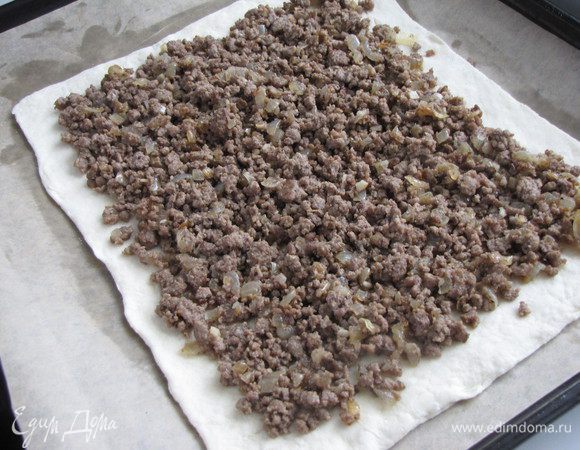 Тесто разморозить. Один лист теста выложить на стол, присыпанный мукой, аккуратно раскатать в прямоугольник. С помощью скалки перенести тесто на противень, застеленный пекарской бумагой. Фарш выложить в центр теста, почти по всей его ширине.