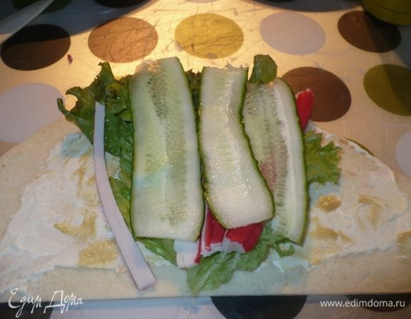 Выложить листья салата, крабовые палочки, огурец.