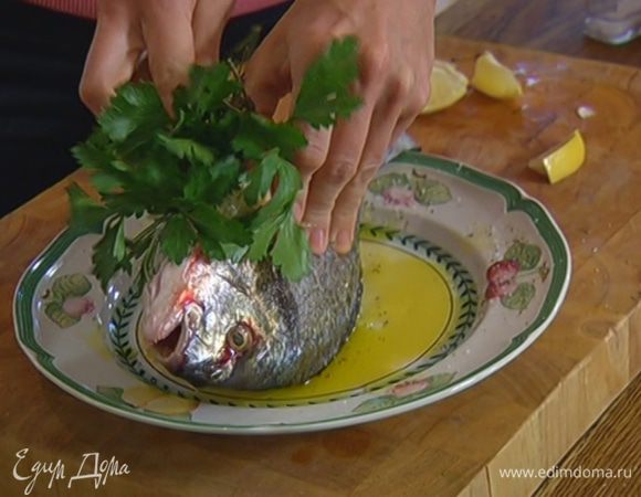 Дораду сбрызнуть оставшимся оливковым маслом, посолить и поперчить со всех сторон. В брюшко рыбы поместить петрушку, розмарин, тимьян и половину долек лимона.