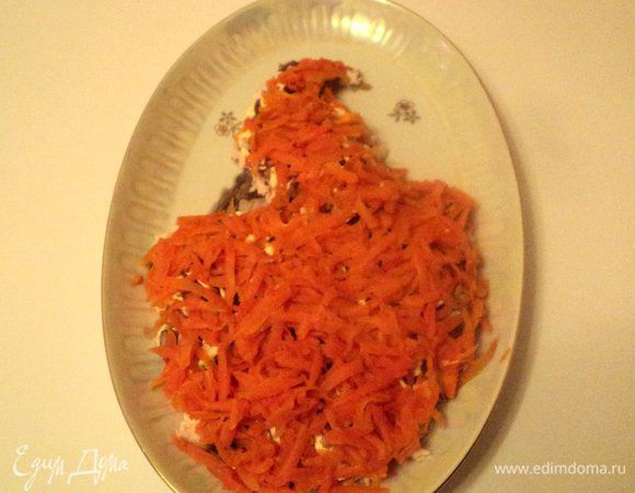 1.5 морковки предварительно отварить, охладить, почистить и натереть на терке. Выложить на грибной слой. Для украшения 0.5 сырой морковки натереть длинными полосками на терке для корейской морковки. Залить на 2-3 минуты горячей водой, затем охладить под холодной водой. 