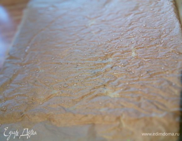 Корж с бумагой перекладываем  на другой лист бумаги, чтобы бумага на которой он пекся была сверху. Слегка ее смочим.  
