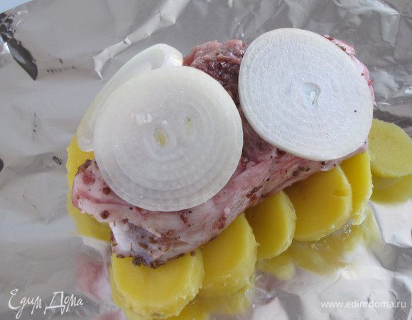 На квадратный лист фольги размером примерно 35х35 см. выложить картофель. Посолить. Накрыть его куском мяса со специями. Поверх мяса выложить лук, нарезанный кольцами, и вновь посолить. Масло добавлять не нужно, т.к. баранина достаточно жирное мясо, оно будет томиться в собственном соку.