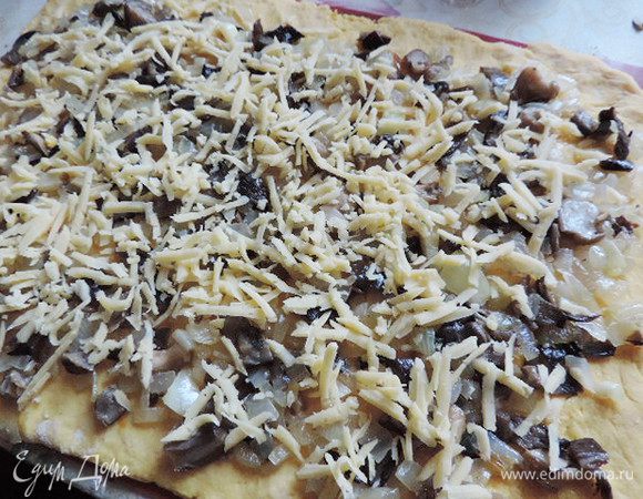 По тесту равномерно распределяем остывшую начинку, не доходя по 2 см до краев. Сверху грибы посыпаем сыром. натертым на крупную терку.