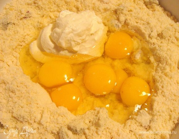 В получившейся массе сделать углубление, разбить туда яйца и добавить сметану.