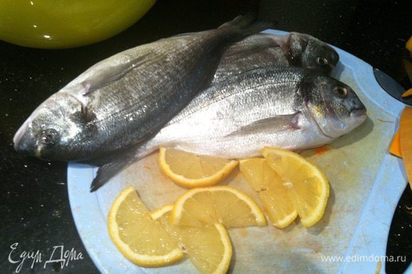 Подготовьте рыбу, хорошо натрите солью и перцем. Половину лимона нарежьте ломтиками.