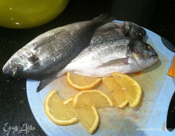 Подготовьте рыбу, хорошо натрите солью и перцем. Половину лимона нарежьте ломтиками.
