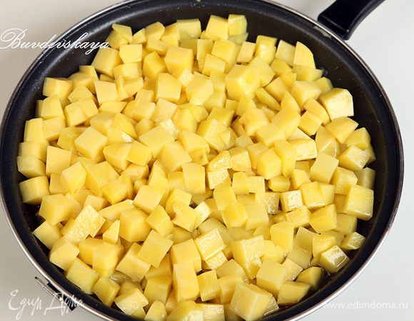 Картофель вымыть, очистить и нарезать кубиками со стороной в 1 см. В сковороде разогреть растительное масло. Не переживайте, что его слишком много: чем больше будет в сковороде масла, тем меньше его в себя впитает картофель, а излишки мы потом сольем. Выложить в сковороду картофель и уменьшить огонь до минимального. Периодически картофель необходимо помешивать лопаткой. Томить до готовности картофеля: он должен стать мягким. Внимание: нам не нужно поджарить картофель до золотистой корочки, нам нужен именно томленный картофель. Это занимает довольно много времени.