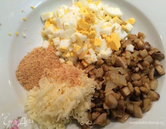 Разогреть в сковороде 2 ст.л. оливкового масла. Чеснок и лук очистить, мелко порезать и обжарить до мягкости. Добавить ножки грибов, жарить 5 минут до золотистого цвета. Снять с огня и остудить.  

Куриное яйцо сварить, остудить, порезать мелким кубиком.
Смешать жареные грибы, яйцо, панировочные сухари, козий сыр.  