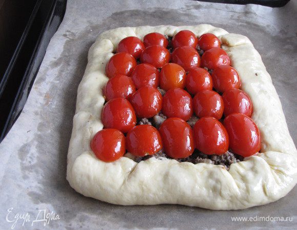 Помидоры черри разрезать пополам, выложить на фарш срезом вниз. Смазать маслом тесто и помидоры.
