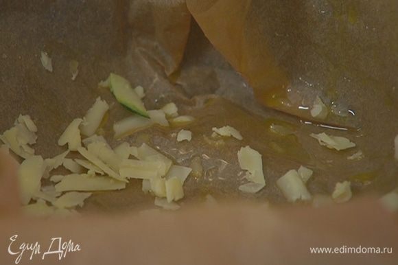 Разъемную форму для выпечки выстелить пищевой бумагой, смазать оставшимся оливковым маслом и посыпать дно частью натертого сыра.