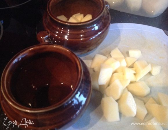 Духовку разогрейте до 180 градусов. Картофель очистите, нарежьте кубиками и разложите по горшочкам.