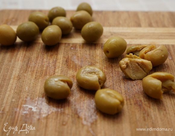 Плоской стороной ножа раздавить оливки, извлечь косточки и нарезать.