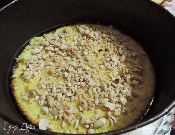 На блюдо кладем первый пласт бисквита, можно еще теплый. Заключаем в кондитерское кольцо или бортик разъемной формы, в которой он выпекался.
Бисквит посыпаем половиной жаренного измельченного арахиса.