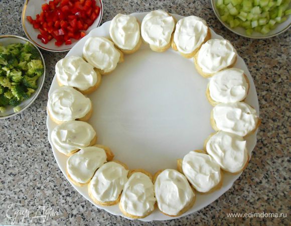 Готовые булочки вместе с бумагой перенесите на решётку и полностью остудите. Подберите блюдо или круглую разделочную доску подходящего диаметра и осторожно переложите венок. Дайте ему соскользнуть с бумаги и он не сломается.

Распределите равномерно сырную смесь поверх булочек.