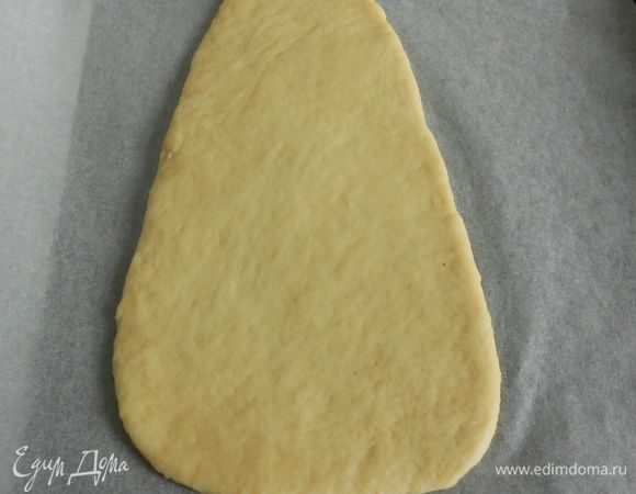 Выложить тесто на присыпанную мукой поверхность, разделить его на 2 неравные части (примерно 2:3). Из  большей раскатать вытянутый треугольник с закругленными углами для головы и шапки. Положите его на пергамент.