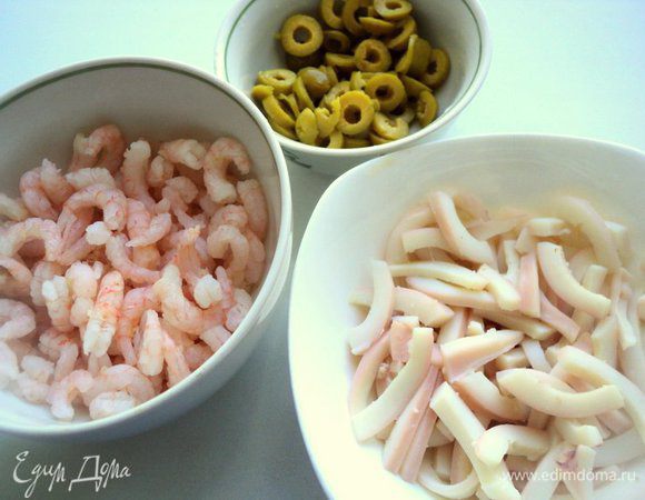 Кальмар ошпарить горячей водой, снять верхнюю пленку. Положить кальмары в подсоленную кипящую воду и варить 2-3 минуты. Охладить кальмары и порезать соломкой. Оливки порезать колечками, вареные креветки разморозить.