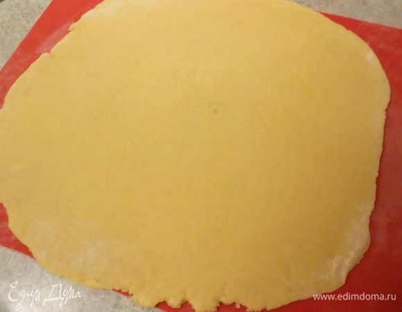 На присыпанной мукой поверхности раскатать остывшее тесто до 35 см в диаметре и перенести на застеленный бумагой противень. 