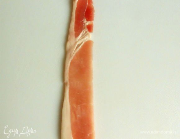 Каждый ломтик бекона разрежьте вдоль. Положите на доску первую полоску бекона,