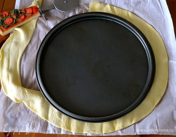 Теперь займемся нижним коржом. Один пласт слоеного теста раскатать и вырезать круг диаметром 26 см. 