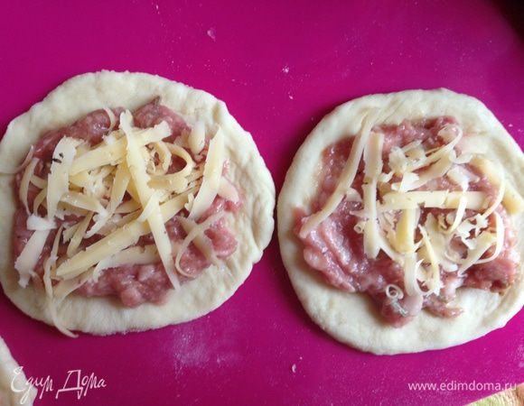 Половину теста раскатать, выдавить стаканом кружки (обрезки собрать и потом снова раскатать, чтобы из них тоже вырезать кружки), на каждый выложить 1 чайную ложку начинки и сверху притрусить тертым сыром.