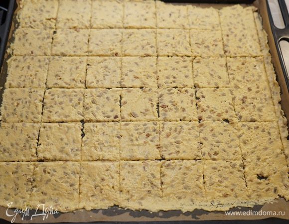 На противень постелить бумагу для выпечки (у меня тефлоновый лист), выложить тесто и аккуратно раскатать как можно тоньше – примерно 2  мм. Тесто очень липкое и можно раскатывать его между двумя листами для выпечки. Ножом нанесите бороздки для разделения кусочков, чтобы по ним потом разломать хлебцы. Посыпать крупной солью.