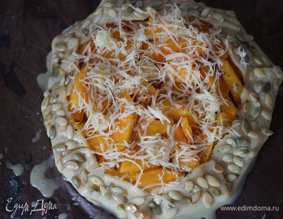 Края теста поднять, защипнуть и уложить на начинку. Сверху положить совсем маленькие кусочки сливочного масла и чуть тёртого сыра. От себя я решила немного украсить галету. Края смазала взбитым желтком и посыпала горстью тыквенных семечек. И это было правильное решение. Как же всё вкусно и хрустяще запеклось!