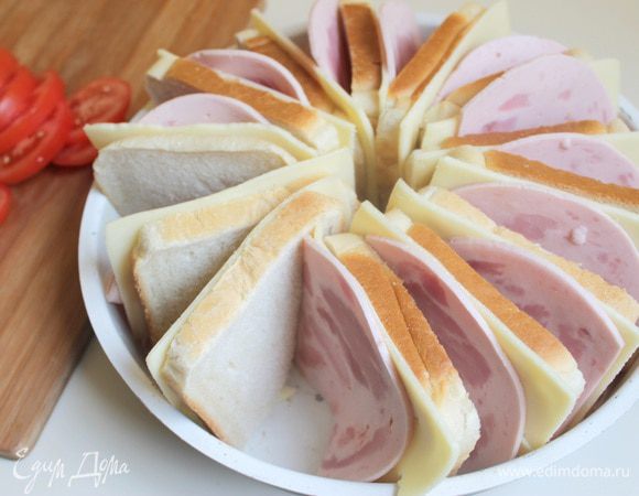 Хлеб слегка смажем маслом. Выкладываем в форму. И между слоями кладем пластинку сыра и пластинку ветчины. Помидоры порежем тонко.