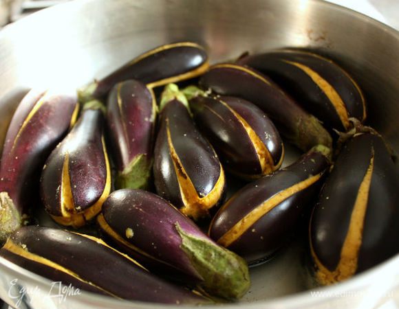 В большой сковороде нагрейте 2 ст.л. масла, выложите баклажаны в один слой и обжаривайте на маленьком огне под крышкой. Для равномерного приготовления периодически переворачивайте их и готовьте до мягкости. 