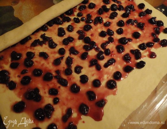 Раскатываем тесто в прямоугольный пласт толщиной около 3-4 мм. Выкладываем вишню с частью сиропа и распределяем ее по тесту равномерно. 