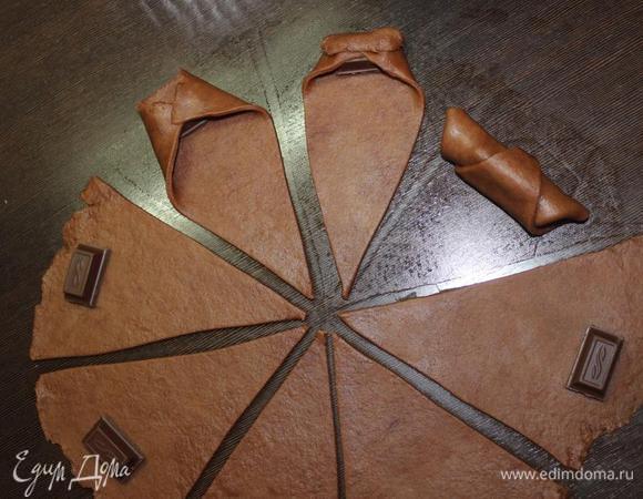 На широкий край выкладываем кусочек шоколада, загибаем края к центру и сворачиваем в рулет к узкому краю.
