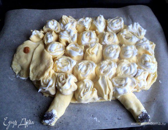 Выложить рулетики в виде барашка на основу. Из кусочка теста вылепить головку и ухо овечки, из тонких рулетиков, смазанных белковым кремом,  ножки. Копытца посыпать маком.