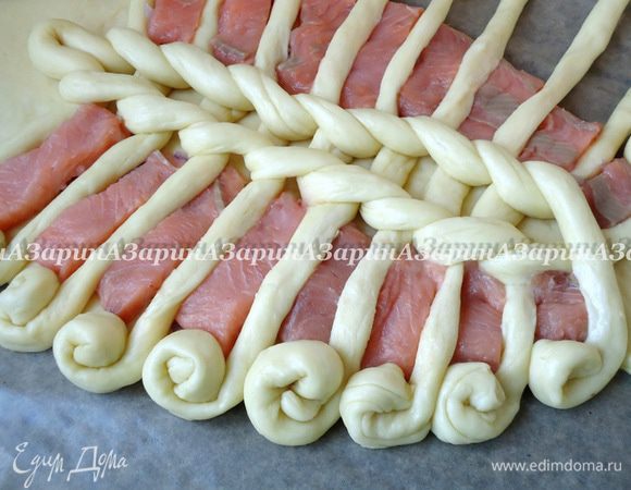 Поверх лука выложить кусочки рыбы, а края жгутов закрутить в вензеля, образуя бортики пирога.