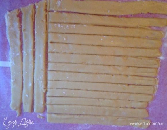 Разделить тесто на 3 части. Каждую из них раскатать на пергаменте в прямоугольный пласт 0,5 см толщиной и нарезать на полоски 2 см шириной, отделить их друг от друга (или после выпекания можно будет прорезать), вместе с пергаментом перенести в разогретую до 220 градусов духовку на несколько минут, до румяности. Горячими подравнять под размер формы.