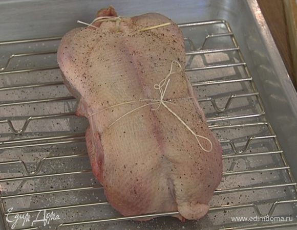 В глубокий противень поместить решетку, сверху выложить утку скрепленным отверстием вверх, затем посолить и поперчить тушку со всех сторон и отправить в разогретую духовку.