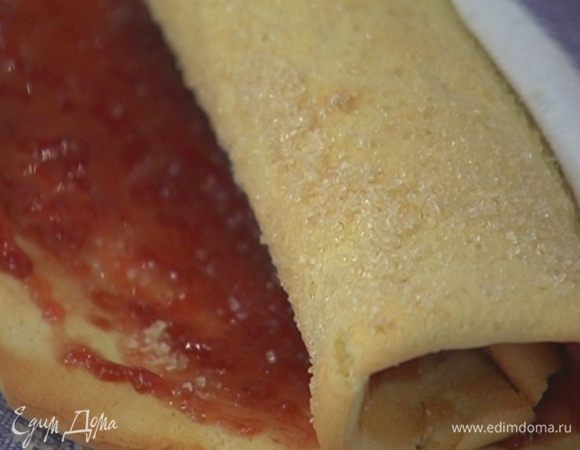 На рабочей поверхности расстелить полотенце, равномерно присыпать его коричневым сахаром, выложить пласт из теста, снять с него бумагу для выпечки и, пока он горячий, смазать тонким слоем малинового варенья, затем при помощи полотенца свернуть в плотный рулет, накрыть его полотенцем и дать отдохнуть.