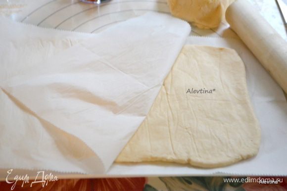 Выложить тесто на рабочую поверхность, застеленную бумагой для выпечки и присыпанную мукой. Помять руками. Разделить тесто на 2 равных куска. Первый кусок раскатаем не тонко (слоем примерно в 1 см) в прямоугольную форму, положив поверх него кусок бумаги для выпечки.