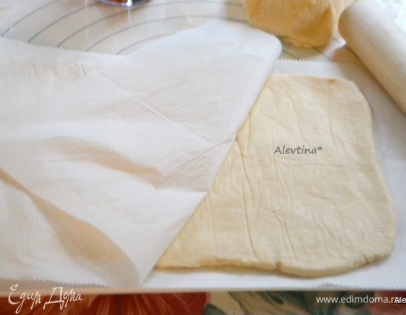 Выложить тесто на рабочую поверхность, застеленную бумагой для выпечки и присыпанную мукой. Помять руками. Разделить тесто на 2 равных куска. Первый кусок раскатаем не тонко (слоем примерно в 1 см) в прямоугольную форму, положив поверх него кусок бумаги для выпечки.