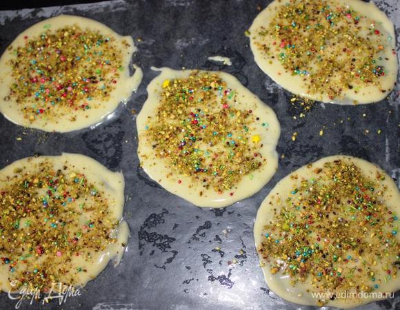 На противень выстилаем пергамент и смазываем его растительным маслом.
Выкладываем по 1 ст. л. теста и размазываем его ложкой в круги диаметром сантиметров 10-12. У меня на противень помещалось по 5 кругов, но для первого раза я рекомендую сделать только 1-2 штуки, чтобы понять, с каким количеством будет удобно работать вам, так как кое-какая скорость и сноровка здесь нужна.
Посыпаем круги фисташками и посыпкой.