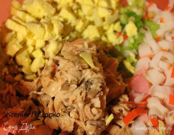 Разделить яйца на белки и желтки. Белки отложить. Желток и крабовые палочки нарезать кубиками, с рыбы слить жидкость и слегка размять ее вилкой, убрав все кости. Зеленый лук мелко нарезать. Белки и морковь натереть на мелкой терке в разные тарелки.