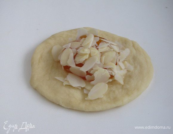 Расплющить шарик в лепешку и выложить 1 ч. л. абрикосового джема, присыпать миндальными лепестками.