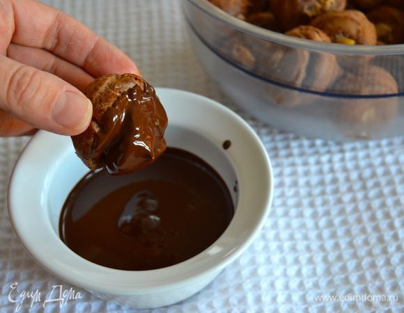 Для шоколадной глазури растопить на водяной бане темный шоколад, перелить в мисочку. Держа профитроли за "основание", обмакивать их верхней частью в шоколадную глазурь. Дать слегка стечь шоколаду и выкладывать профитроли на решетку до полного застывания глазури.  