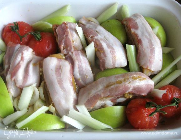 На верхнюю часть каждого куска положить полоску бекона. Положить лук в форму в промежутки между кусками мяса, яблоко с кожурой (кожурой вверх), разрезанное на восьмушки (семенную часть предварительно удалить), стебель сельдерея, порезанный на кусочки, помидоры.
