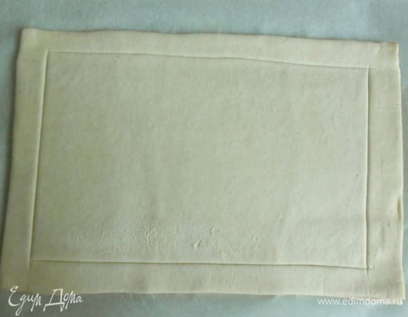 Слегка раскатайте примерно до 20х30 см. Делайте это сразу на пекарской бумаге. Отступите от краёв на 2 см и очень поверхностно прорежьте ножом. Внутренний прямоугольник часто наколите вилкой. Переложите тесто вместе с бумагой на противень и выпекайте 5-7 минут. Тесто должно хорошо "раскрыться", но не подрумянивайте его. (Первый раз я делала пирог без этого предварительного запекания и низ мне показался сырым, да и бортики без прорезей деформировались.)