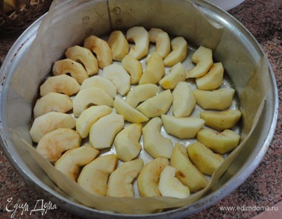 Яблоки очистить от кожуры и сердцевины и каждое разрезать на 8 частей. Форму полностью выстлать пекарской бумагой и смазать ее растительным маслом. Выложить половинки яблок.