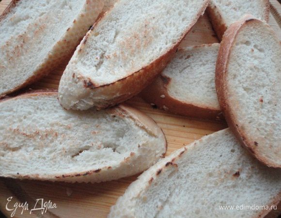 Багет нарезать ломтиками и слегка обжарить на сухой сковороде. 
Ломтик чеснока надрезать и натереть им каждый ломтик багета.