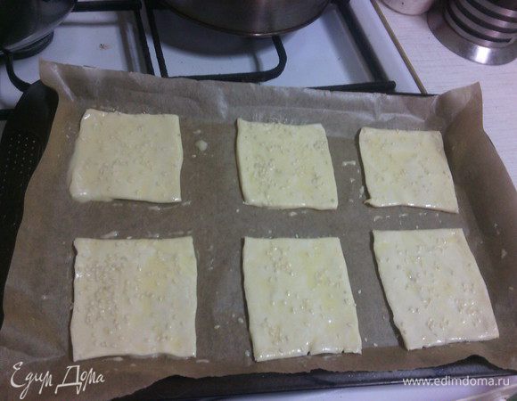 Слоеное тесто разморозить, разрезать на квадраты, выложить на противень, застеленный пергаментом.
Из данного количества теста получится много порций, поэтому часть можно использовать, например, для пирожков или сладких пирожных.

Смазать яичным желтком, можно посыпать кунжутом.