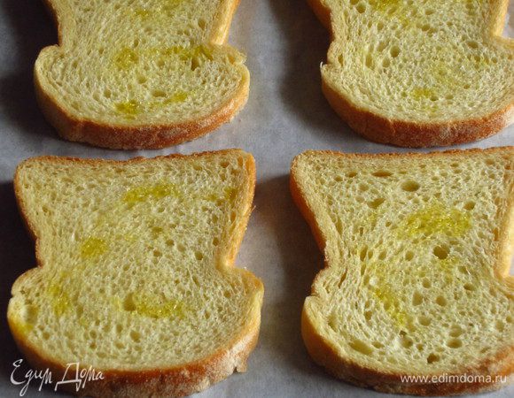 Ломтики хлеба сбрызнуть оливковым маслом, выложить на противень с пергаментом и запечь в разогретой до 180 С духовке 6 минут.